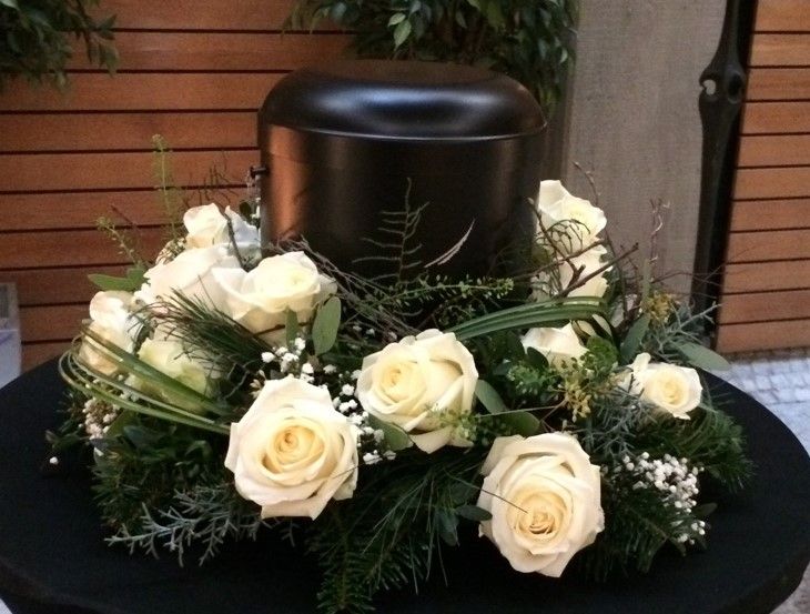 Schwarze Urne mit weißen Rosen auf floralem Trauerarrangement